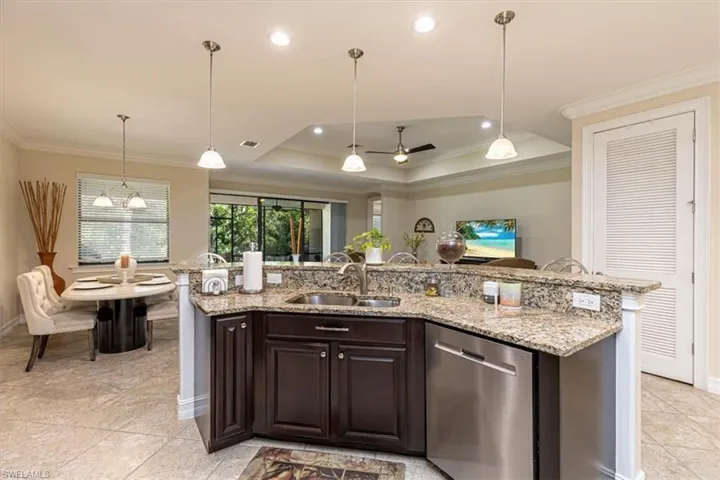 Kitchen with ornamental molding, a tray ceiling, dark brown cabinets, pendant lighting, and dishwasher