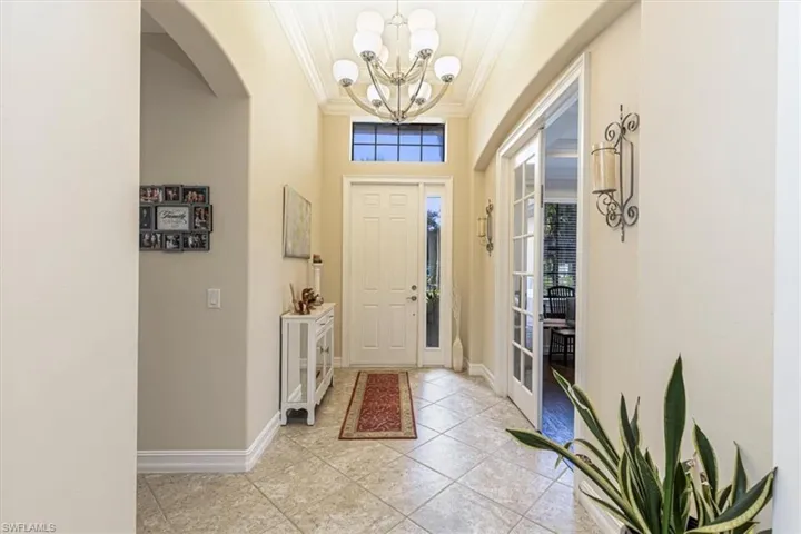 Entryway with ornamental molding, arched walkways, a chandelier, and light tile patterned floors