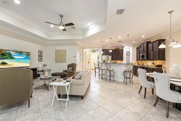 Living room with a raised ceiling, crown molding, ceiling fan, recessed lighting, and a chandelier