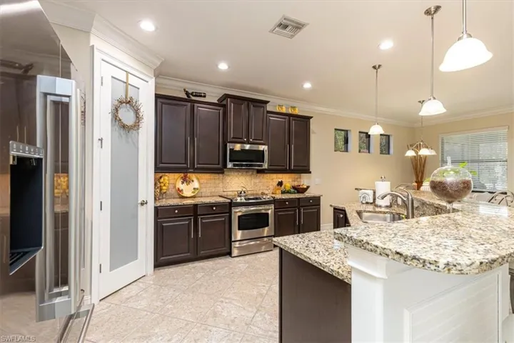 Kitchen featuring dark brown cabinetry, appliances with stainless steel finishes, hanging light fixtures, crown molding, and decorative backsplash