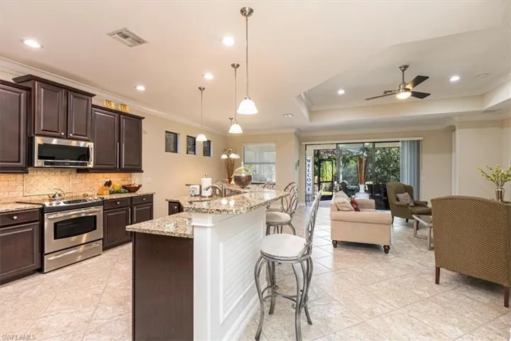Kitchen with dark brown cabinets, stainless steel appliances, a breakfast bar area, crown molding, and pendant lighting