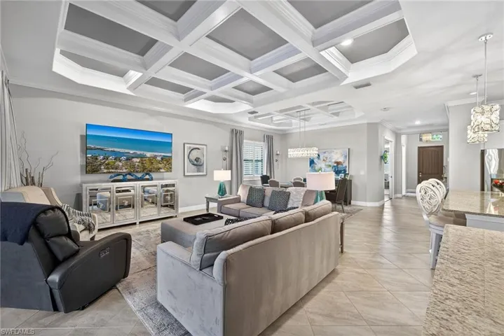 Living area featuring coffered ceiling, crown molding, light tile patterned flooring, and hanging lights