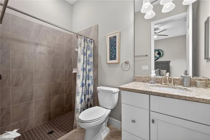 Ensuite bathroom with a textured wall, vanity, a stall shower, and a ceiling fan