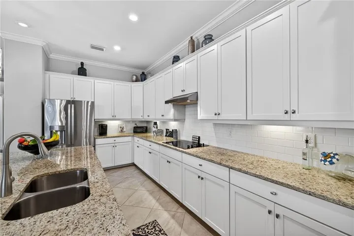 Kitchen with white cabinetry, crown molding, stainless steel fridge with ice dispenser, backsplash, and light stone countertops