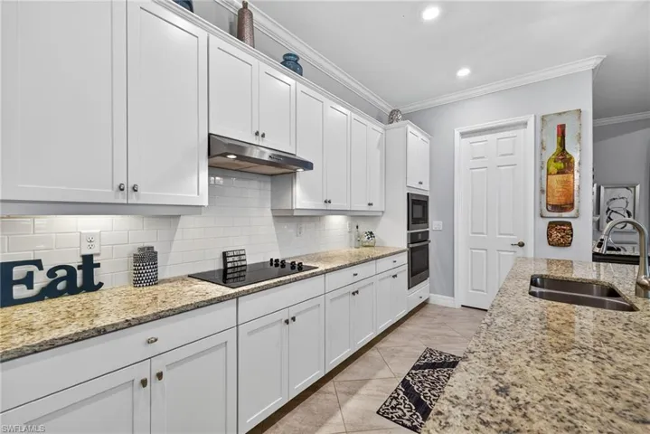 Kitchen with crown molding, white cabinets, light stone countertops, stainless steel oven, and black electric stovetop