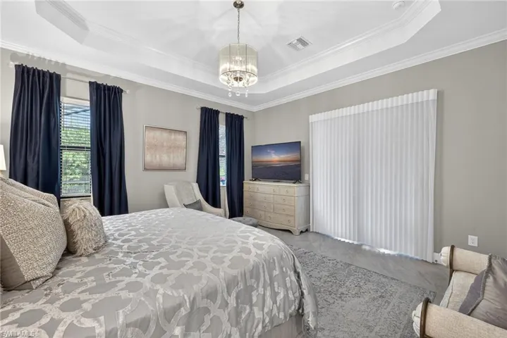 Bedroom with suspended lighting, multiple windows, a raised ceiling, and ornamental molding