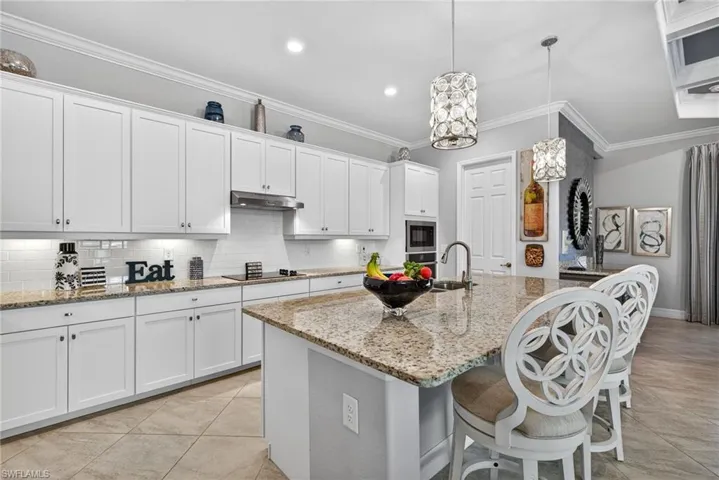 Kitchen featuring white cabinets, light stone countertops, a center island with sink, a kitchen breakfast bar, and ornamental molding