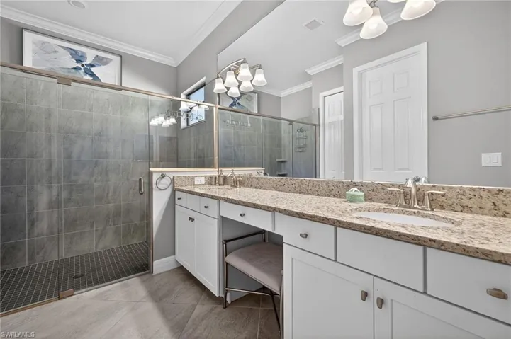 Full bath featuring double vanity, a shower stall, suspended lighting, and crown molding
