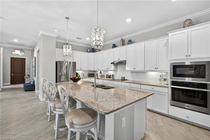 Kitchen featuring stainless steel appliances, a breakfast bar area, light stone counters, white cabinets, and a center island with sink