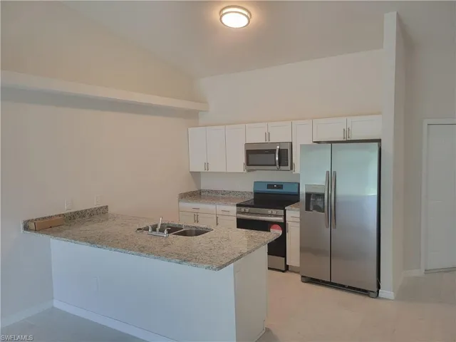 Kitchen featuring white cabinets, appliances with stainless steel finishes, kitchen peninsula, and lofted ceiling