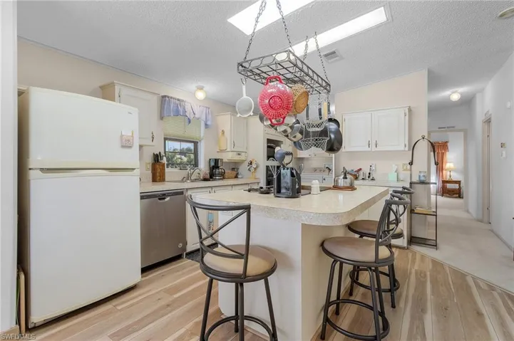 Kitchen with a skylight, light countertops, stainless steel dishwasher, freestanding refrigerator, and a kitchen breakfast bar