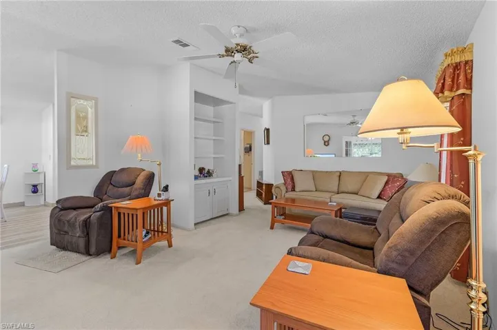 Living area with light carpet, ceiling fan, built in shelves, and a textured ceiling