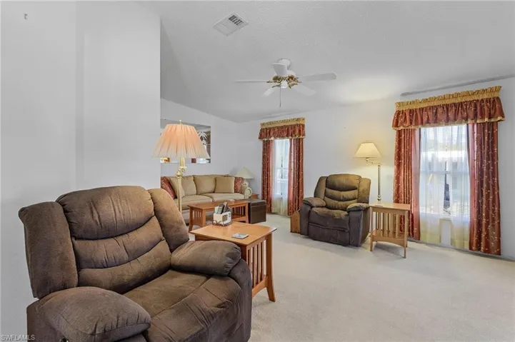 Living area with visible vents, a ceiling fan, light carpet, vaulted ceiling, and a textured ceiling