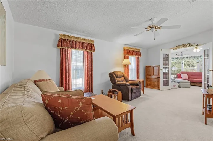 Living room featuring a ceiling fan, vaulted ceiling, a textured ceiling, french doors, and carpet floors
