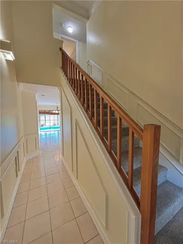 Stairs featuring a decorative wall, wainscoting, crown molding, and tile patterned flooring