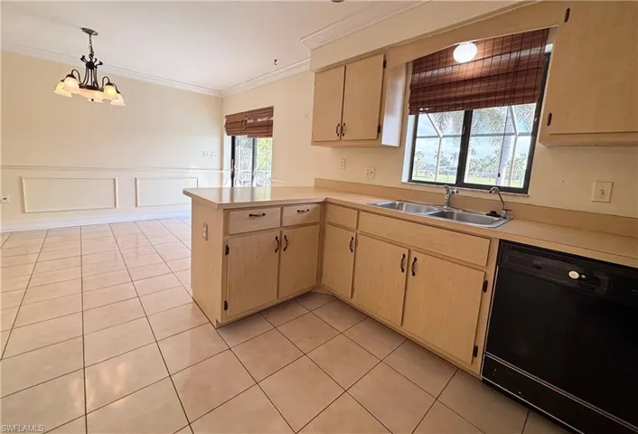 Kitchen with light brown cabinets, dishwasher, light countertops, light tile patterned floors, and a decorative wall