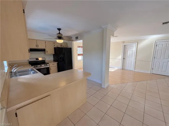 Kitchen with black refrigerator with ice dispenser, light tile patterned floors, crown molding, stainless steel range with electric stovetop, and light countertops