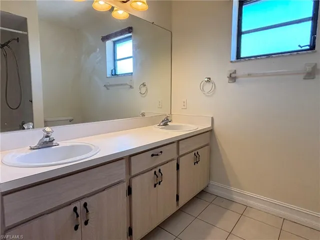 Bathroom featuring double vanity, light tile patterned floors, and a shower