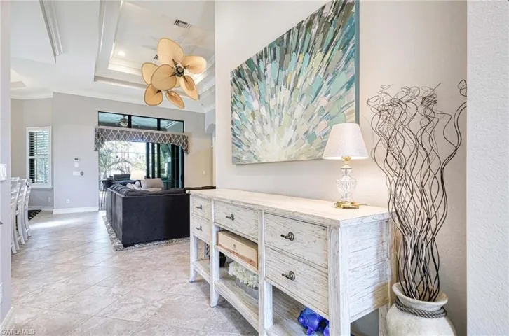 Hallway with light tile patterned floors, a tray ceiling, and crown molding