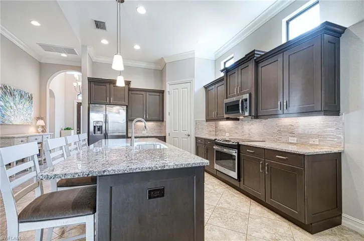 Kitchen featuring ornamental molding, stainless steel appliances, sink, pendant lighting, and an island with sink