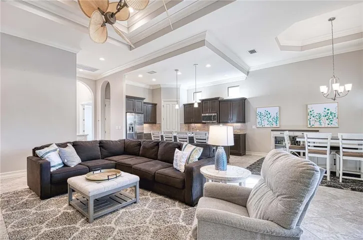 Tiled living room featuring ceiling fan with notable chandelier, a raised ceiling, and crown molding