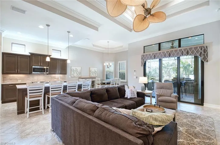 Tiled living room featuring a tray ceiling, ceiling fan, and ornamental molding