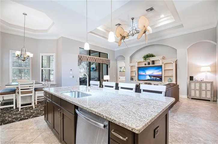 Kitchen featuring sink, light stone counters, stainless steel dishwasher, a chandelier, and a kitchen island with sink