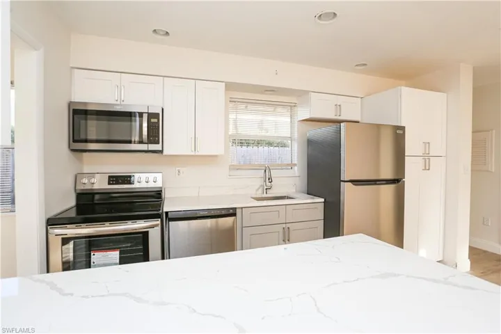 Kitchen featuring white cabinets, light hardwood / wood-style floors, light stone countertops, sink, and stainless steel appliances