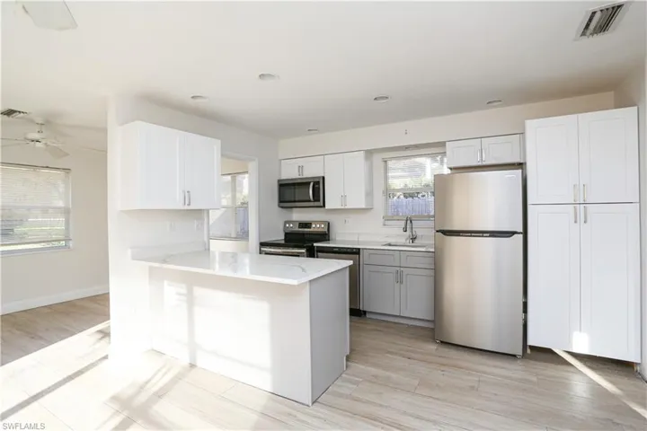 Kitchen with stainless steel appliances, light hardwood / wood-style floors, white cabinetry, sink, and ceiling fan