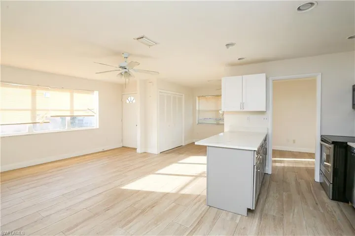 Kitchen with ceiling fan, white cabinets, light wood-type flooring, and light stone countertops