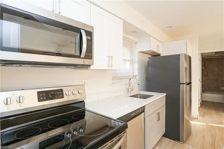 Kitchen featuring sink, light hardwood / wood-style flooring, light stone countertops, stainless steel appliances, and white cabinets
