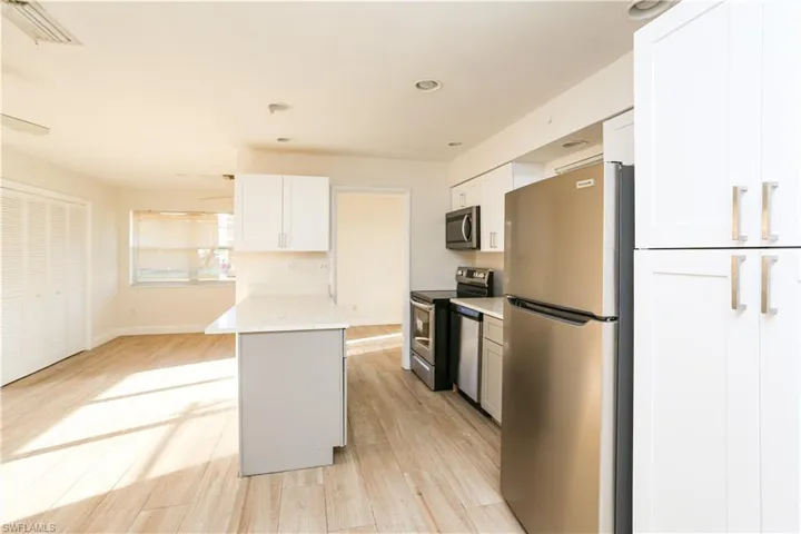 Kitchen with stainless steel appliances, white cabinetry, light stone counters, light wood-type flooring, and a kitchen island