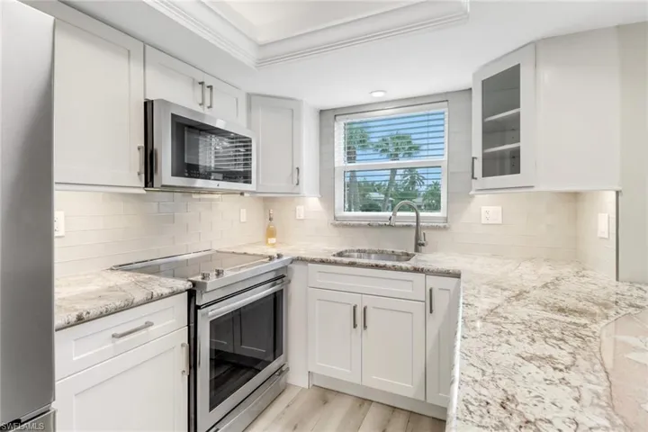 Bright kitchen featuring appliances with stainless steel finishes, and white cabinets and an elegant granite countertop
