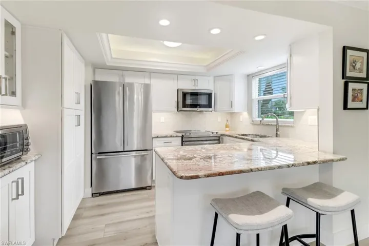 Kitchen featuring sink, white cabinets, a raised ceiling, and stainless steel appliances