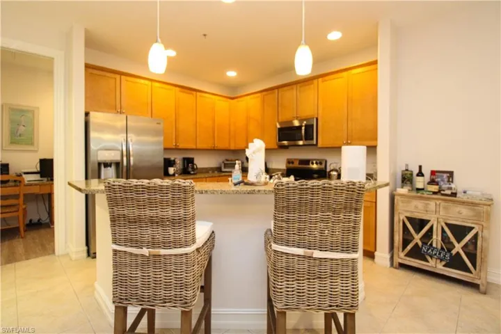 Kitchen featuring light stone countertops, appliances with stainless steel finishes, light tile patterned floors, and hanging light fixtures