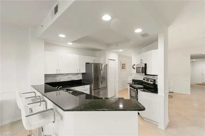 Kitchen featuring backsplash, white cabinets, a kitchen breakfast bar, stainless steel appliances, and dark stone countertops