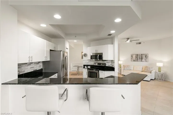 Kitchen featuring white cabinetry, stainless steel appliances, backsplash, dark stone countertops, and a tray ceiling