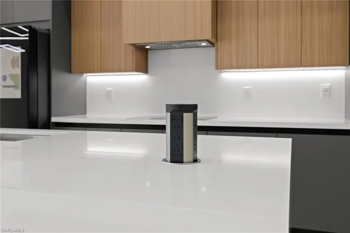 Kitchen view of modern cabinets, light countertops, under cabinet range hood, and light brown cabinets