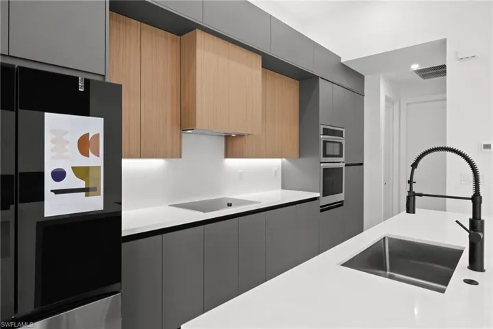 Kitchen with black electric stovetop, modern cabinets, light countertops, stainless steel double oven, and freestanding refrigerator