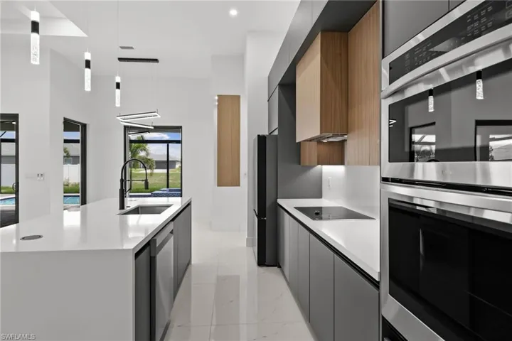 Kitchen with modern cabinets, stainless steel appliances, a center island with sink, light countertops, and pendant lighting
