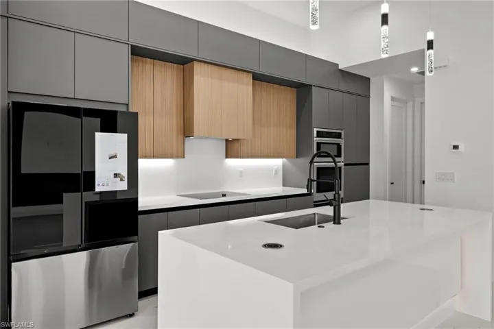 Kitchen featuring smart refrigerator, black electric cooktop, modern cabinets, and a center island with sink