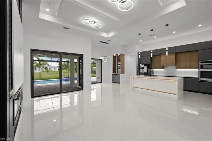 Kitchen with modern cabinets, a raised ceiling, light marble finish flooring, and recessed lighting