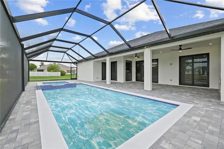 View of swimming pool featuring ceiling fan, a pool with connected hot tub, a patio area, and glass enclosure