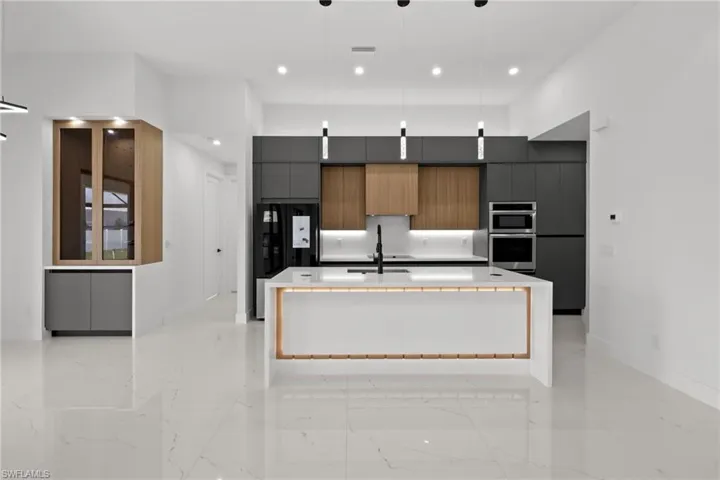 Kitchen with modern cabinets, double oven, freestanding refrigerator, a spacious island, and light marble finish floors