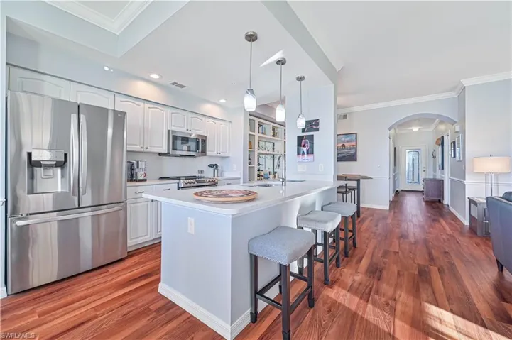 Kitchen with appliances with stainless steel finishes, a kitchen island with sink, hardwood / wood-style flooring, decorative light fixtures, and white cabinets