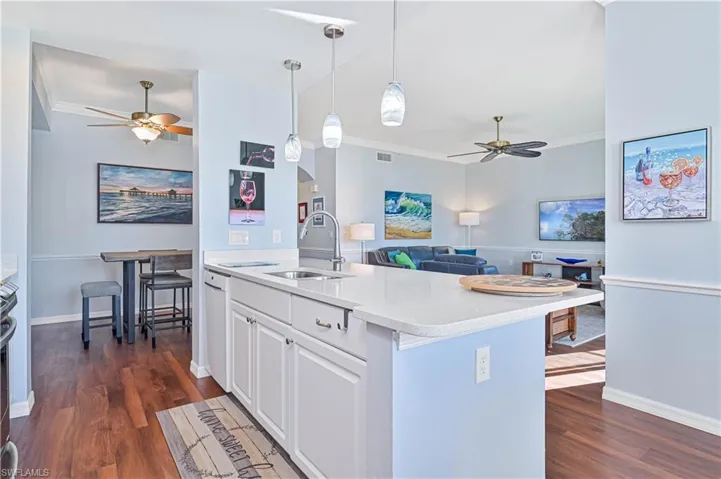 Kitchen with dark hardwood / wood-style flooring, a kitchen island with sink, sink, white cabinets, and hanging light fixtures