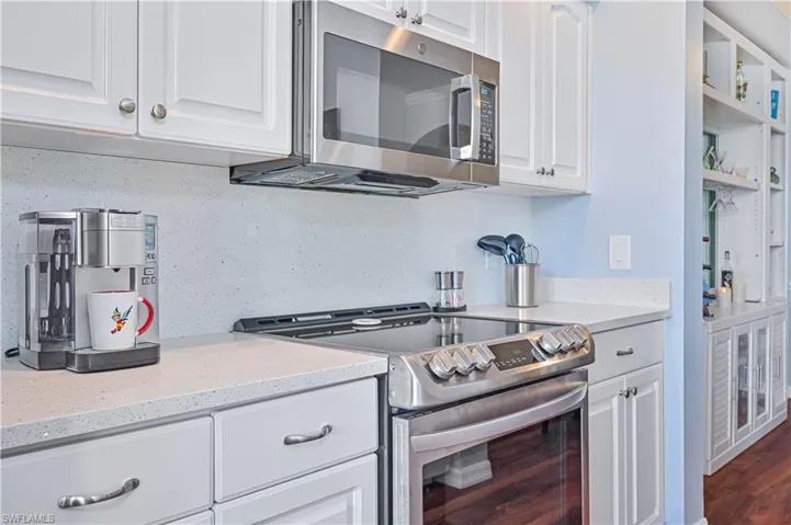Kitchen with dark wood-type flooring, tasteful backsplash, light stone counters, white cabinetry, and stainless steel appliances