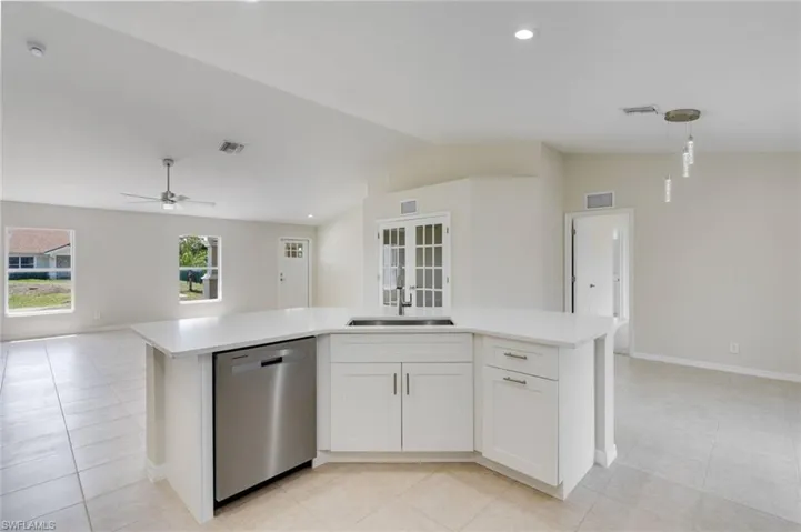 Kitchen with a center island with sink, open floor plan, stainless steel dishwasher, lofted ceiling, and white cabinetry
