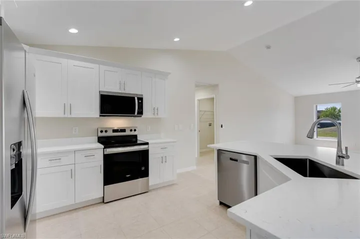Kitchen featuring stainless steel appliances, white cabinets, lofted ceiling, light stone countertops, and recessed lighting