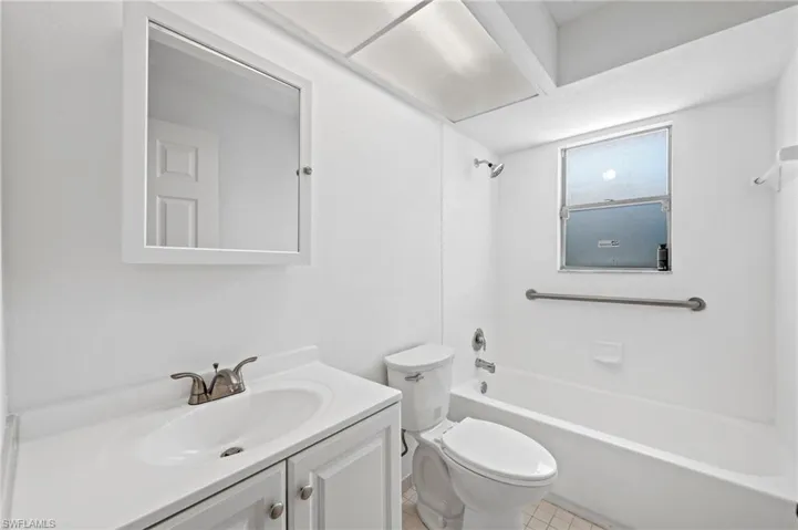 Bathroom featuring a white vanity with integrated sink, mounted mirror, and a shower-tub combination with a window